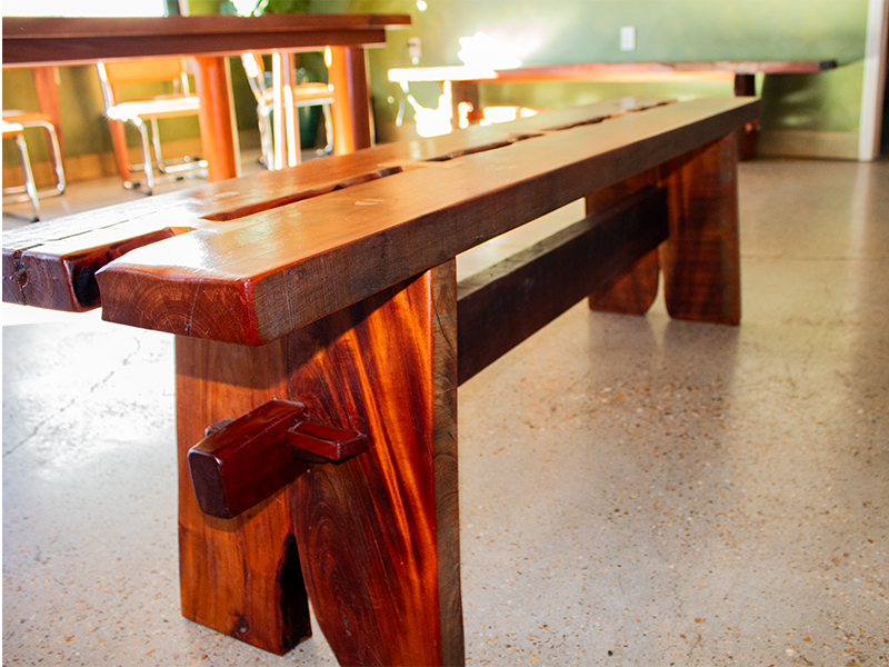 Mahogony split top bench using traditional joinery, with Maple and Purple Heart bowtie inlays, end view in an indoor natural setting.