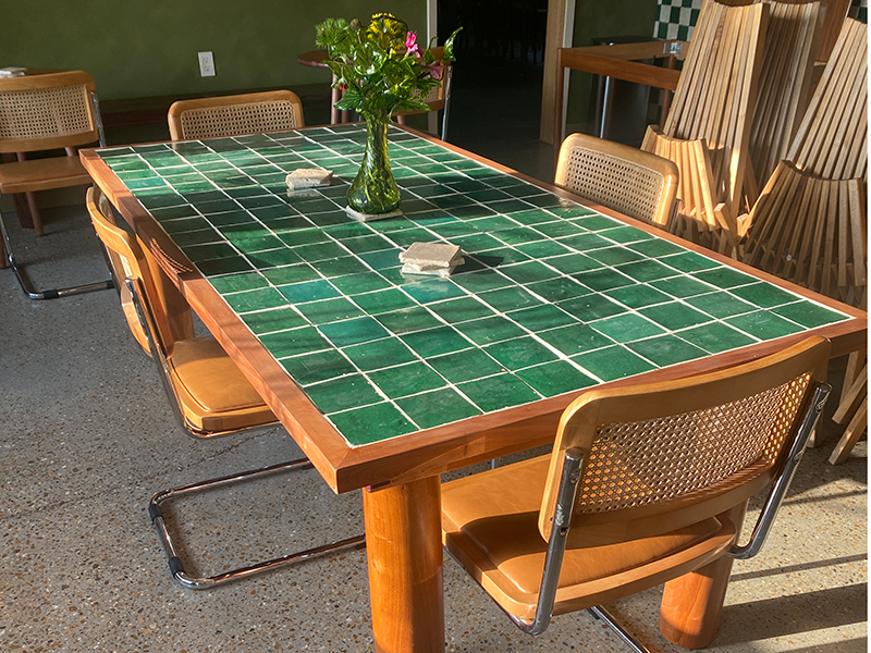 Mahogany dining table with green tile top including hand shaped cylindrical legs and Purple Heart miter spline accents, shown in a natural setting at Common Ground Coffiee shop.
