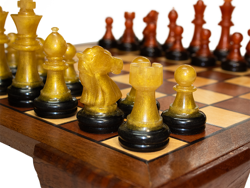 Chessboard made from Mahogany and Hard Maple with an Ipe border and Spanish Cedar feet and black resin lines,  corner view close up of gold resin chess pieces.